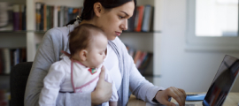 mother holding baby, using laptop