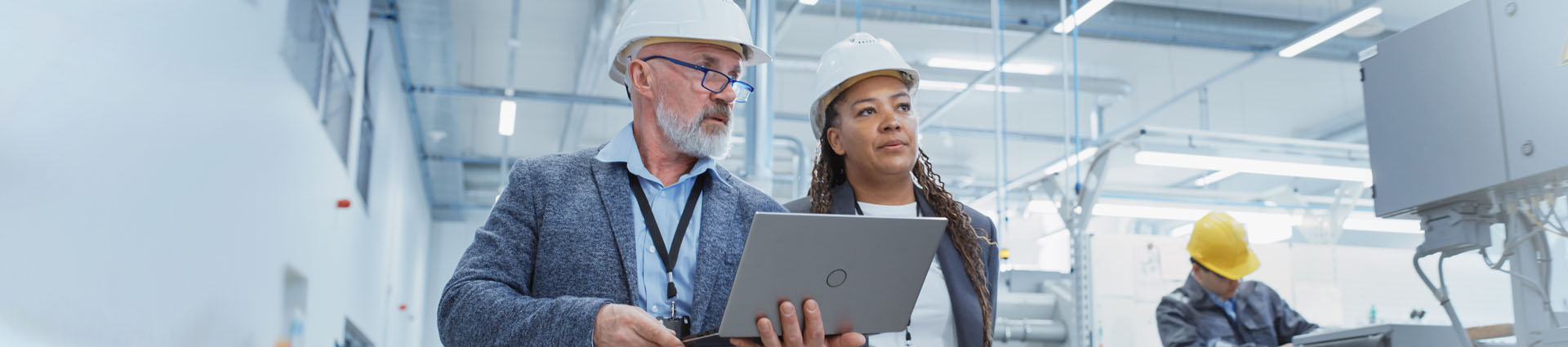 one woman in a hard hat and one woman with laptop walking through factory floor conducting an energy analysis